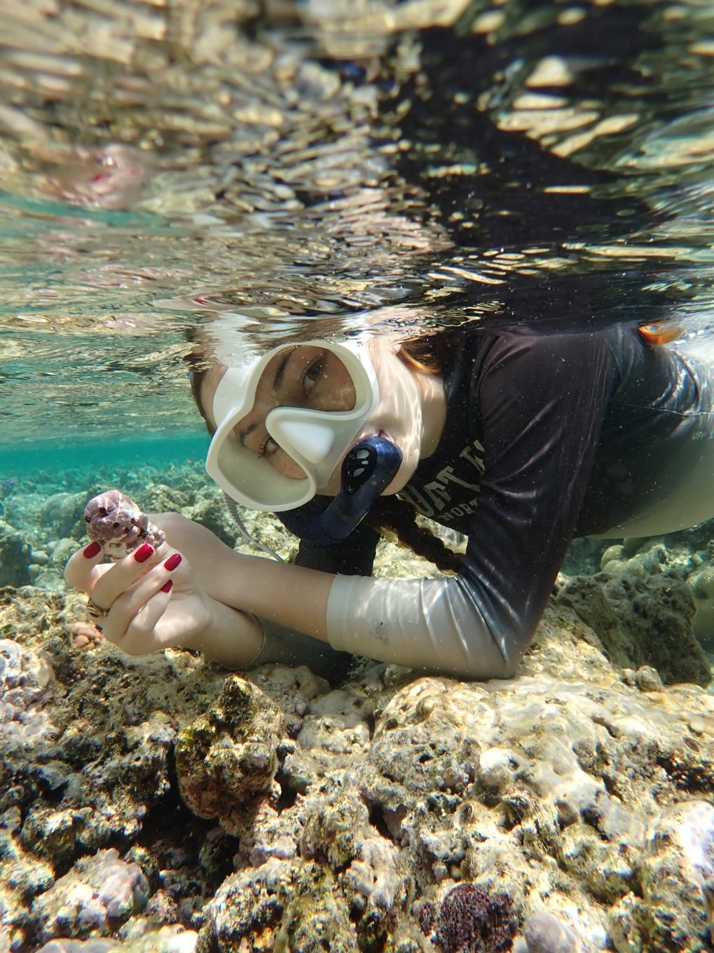 Junge Frau mit Taucherbrille (unter Wasser) hält einen Rhodolithen in der Hand