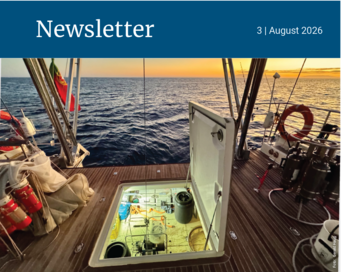 View of a boat deck with an open hatch revealing equipment below, set against a sunset over the ocean.