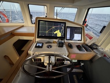 Steuerstand mit Navigationsbildschirm und Steuerrad auf einem Boot bei ruhiger See.